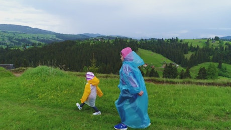 Happy sisters walking through the field wearing raincoats.