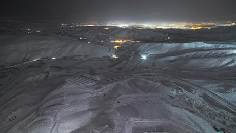Hills covered in snow with the city lights in the background