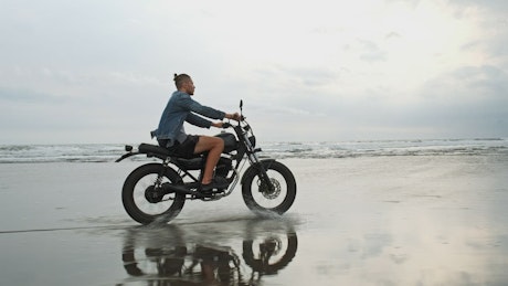 Hipster biker riding a motorcycle near the seashore.