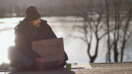Homeless man on the street with a cardboard sign.