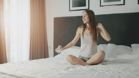 Hopeful young woman stretches on bed to morning sunshine.