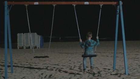 Kid alone on a beach swing.