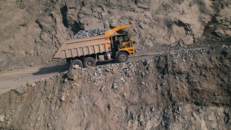 Large yellow dump truck filled with rocks driving in a quarry.