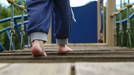 Legs of a child walking barefoot on play bridge.