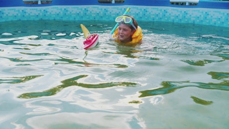 Little boy swimming in a pool with a toy boat.
