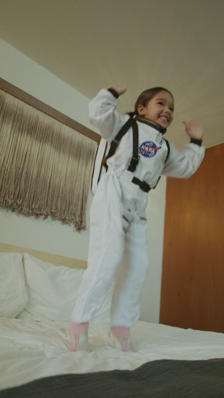 Little girl dressed as an astronaut jumping on the bed.