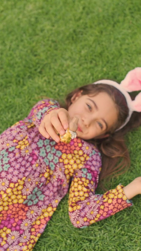 Little girl laying in the grass enjoying a chocolate bunny.
