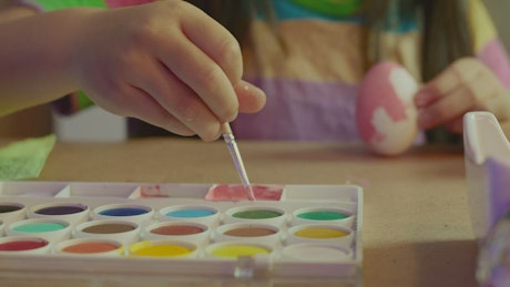 Little girl painting an egg with pink paint.