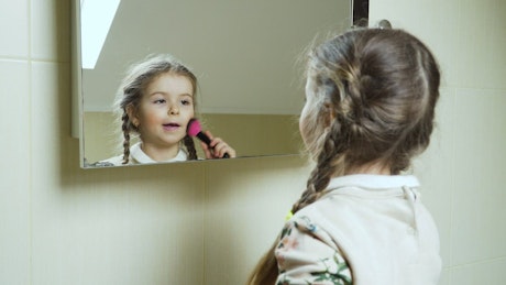 Little girl playing makeup in the mirror