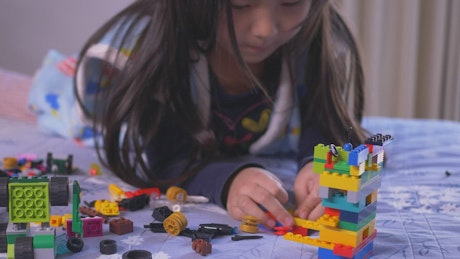 Little girl playing on her bed with legos.