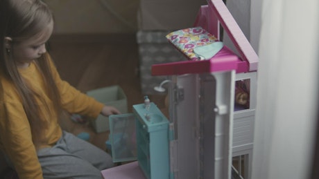 Little girl playing with a dollhouse in her room.