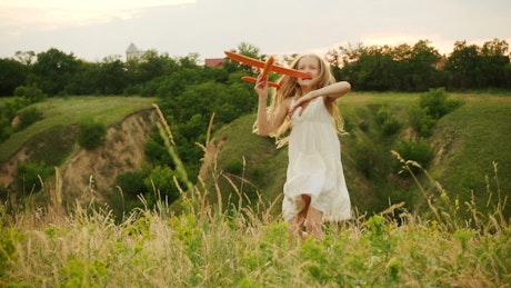 Little girl throwing a toy plane In the hills.
