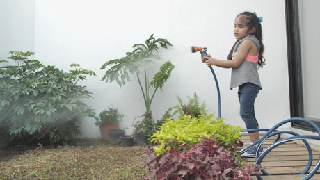 Little girl watering her home garden with a hose.