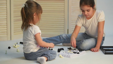 Little sisters playing chess on the floor.