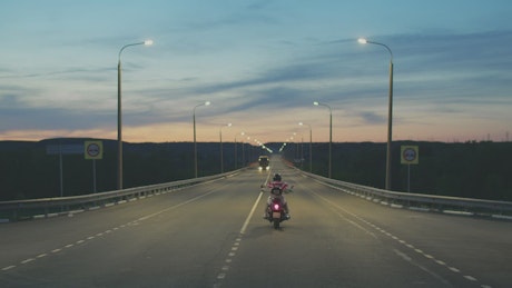 Lone motorcyclist driving down the highway at night.