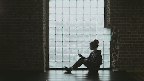 Lonley girl sitting on floor with headphones backlit by window.