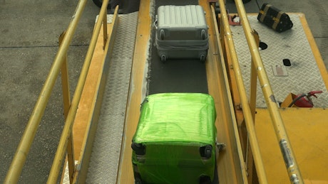 Luggage moving down a conveyer belt loading onto a plane.