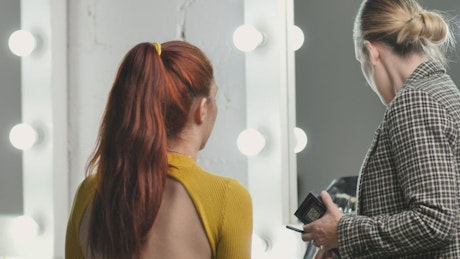 Makeup artist putting makeup on a model in front of a mirror