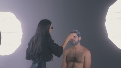 Makeup artist retouching a man's white hair.