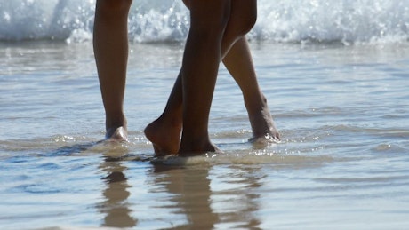 Male and female feet are standing on the sandy beach.