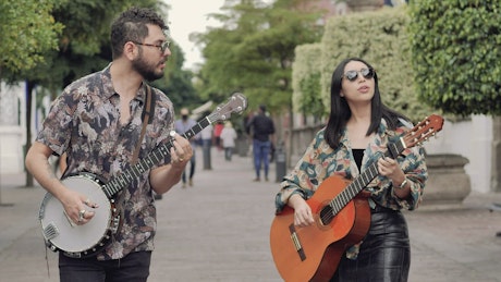 Male and female friends walking through a park while playing music.