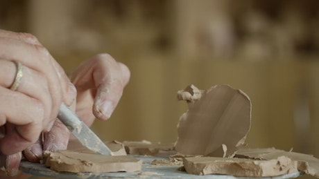 Male hands working on clay with cutting tools.
