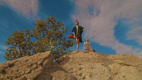 Man and woman doing yoga on a huge rock.