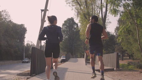 Man and woman jogging through a park in the city.