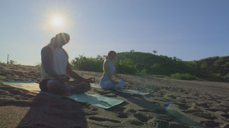 Man and woman meditating on the sand.