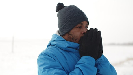 Man blowing air into his cupped hands to warm up in the cold.