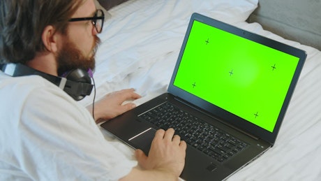 Man browses greenscreen website on laptop in bed.