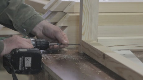 Man building a wooden frame using a power drill.