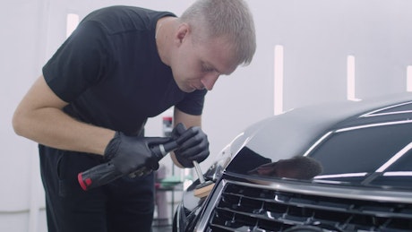 Man carefully polishing the front of a shiny car.