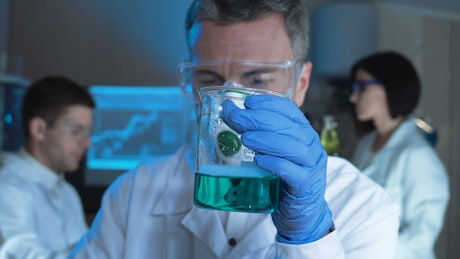 Man checking a chemical flask with blue liquid.