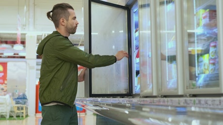 Man chooses products from supermarket refrigerators.
