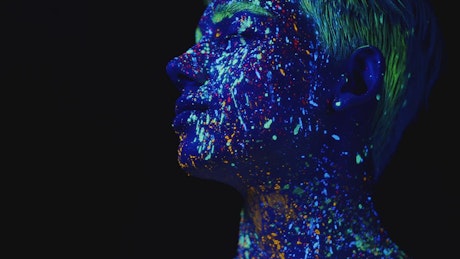 Man covered in neon paint standing under UV light.