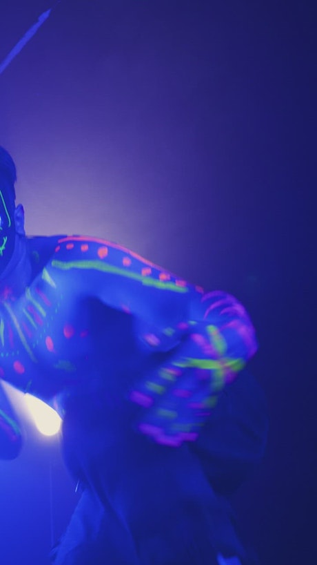 Man dancing with fluorescent paint and a mask.