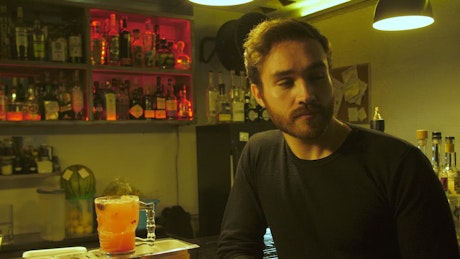 Man drinking a prepared red drink in a bar.