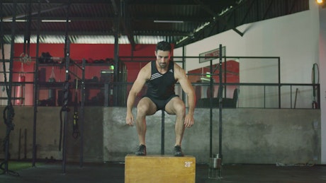 Man exercising by jumping onto a platform in a gym.