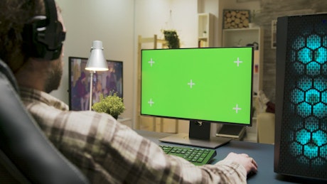 Man gaming at home with green screen monitor.