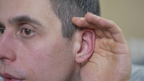 Man hard of hearing cupping his ear.