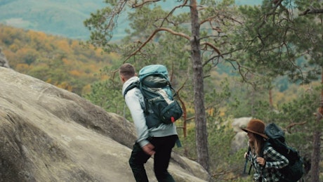 Man helps girlfriend climb up rock during hike.