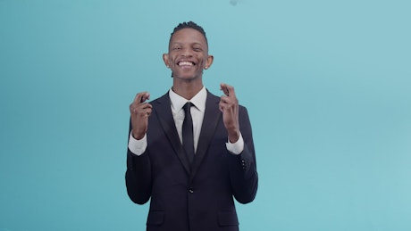 Man in a suit crossing his fingers in luck against a blue background.