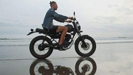 Man in denim jacket riding motorcycle on beach