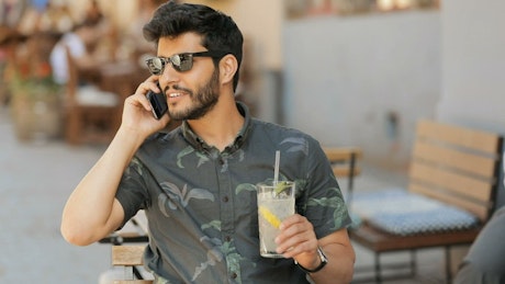 Man in sunglasses talks on mobile holding lemonade