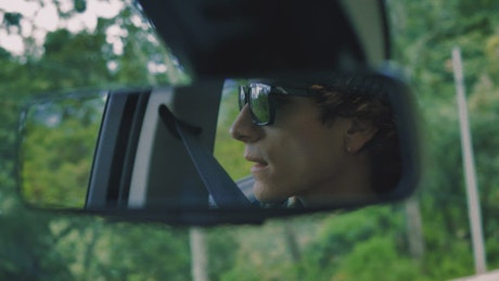 Man in the rear view mirror traveling through a forest.