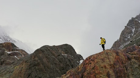 Man in yellow coat cheers on mountain ridge.