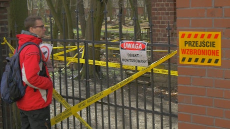 Man looking at a closed fence with warning signs.