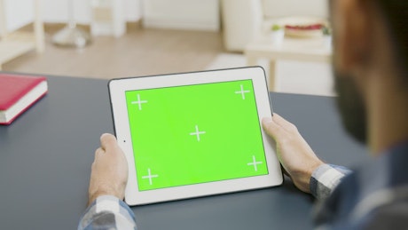 Man looking at a tablet with green screen.
