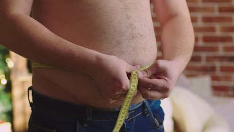 Man measuring his stomach with a tape measure.